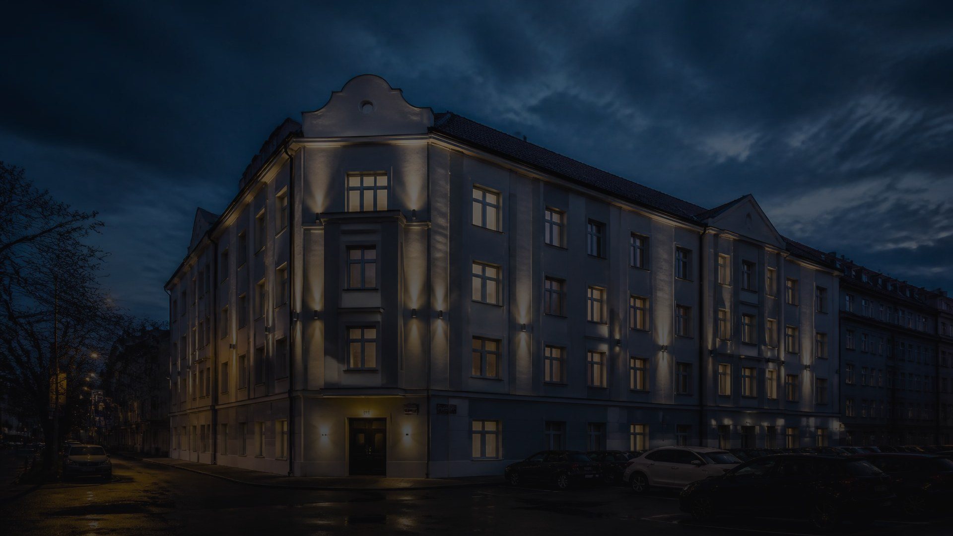 Osvětlený činžovní dům na nároží ve večerních hodinách